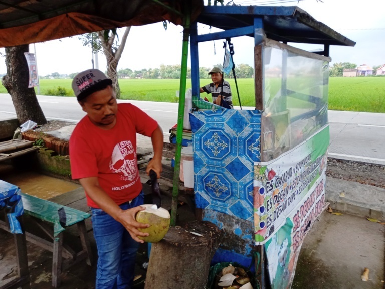 PASRAH: Giyar, pedagang es kelapa muda di pinggir jalan raya Kebakkramat-Tasikmadu, Karanganyar. (PUJOKO/KORAN LINGKAR JATENG)
