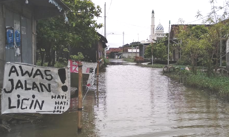 PARAH: Tulisan 'awas jalan licin' di area jalanan yang tergenang air selama 3 bulan di Dukuh Bransong, Desa Banjarsari, Kecamatan Sayung, Demak. (ADITIA ARDIAN/KORAN LINGKAR JATENG)