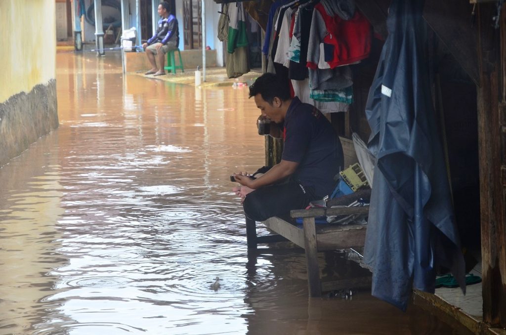 Warga duduk di depan rumahnya yang tergenang banjir di Desa Kesambi, Mejobo, Kudus, Jawa Tengah, Selasa (19/1/2021). (KORAN LINGKAR JATENG/LINGKAR.CO)