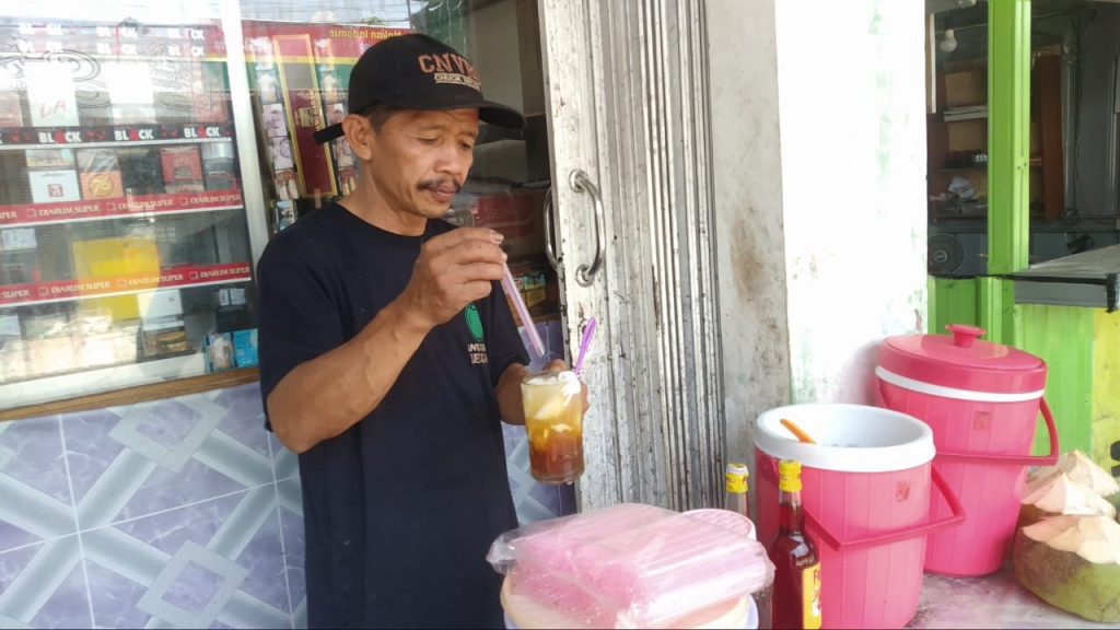 Penjual kelapa muda, Martono sedang melayani pembeli. FOTO: DANANG DISKA ATMAJA/Lingkar.co